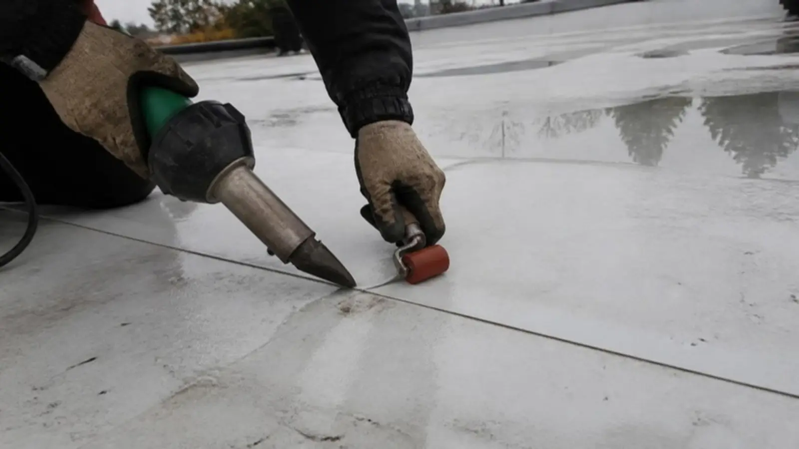 Roofer heat-welding a seam on a white TPO membrane on a wet flat commercial roof